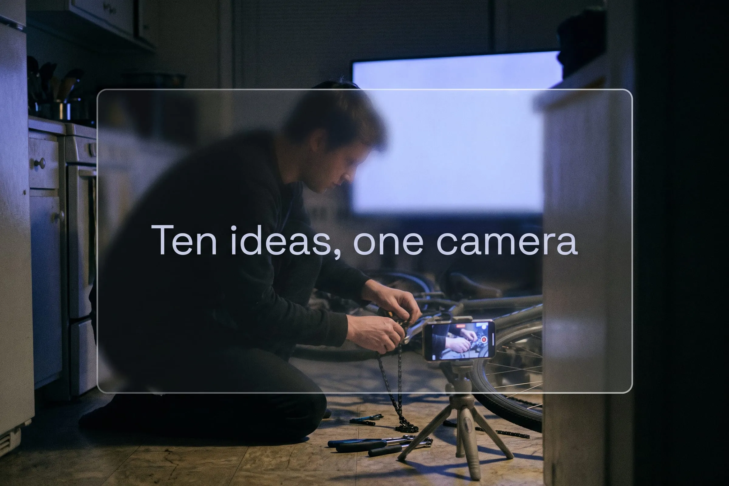A person films their hands fixing a bike chain on a phone mounted to a small tripod on the floor.