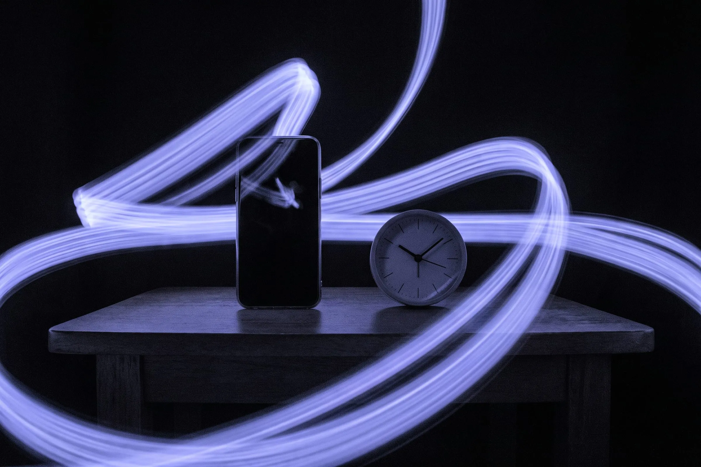 A phone standing upright next to a small clock, ringed by streaks of moving light.