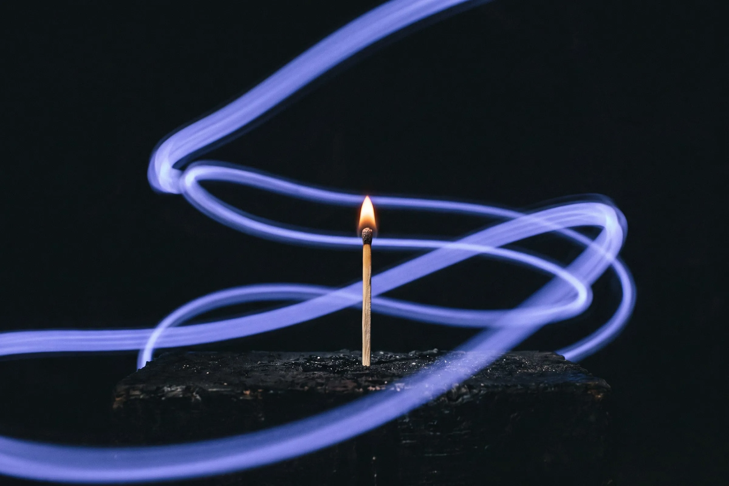 A single upright lit match with streaks of light spreading outward around it.