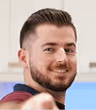 Portrait of a smiling man with short brown hair and a beard, wearing a maroon shirt.